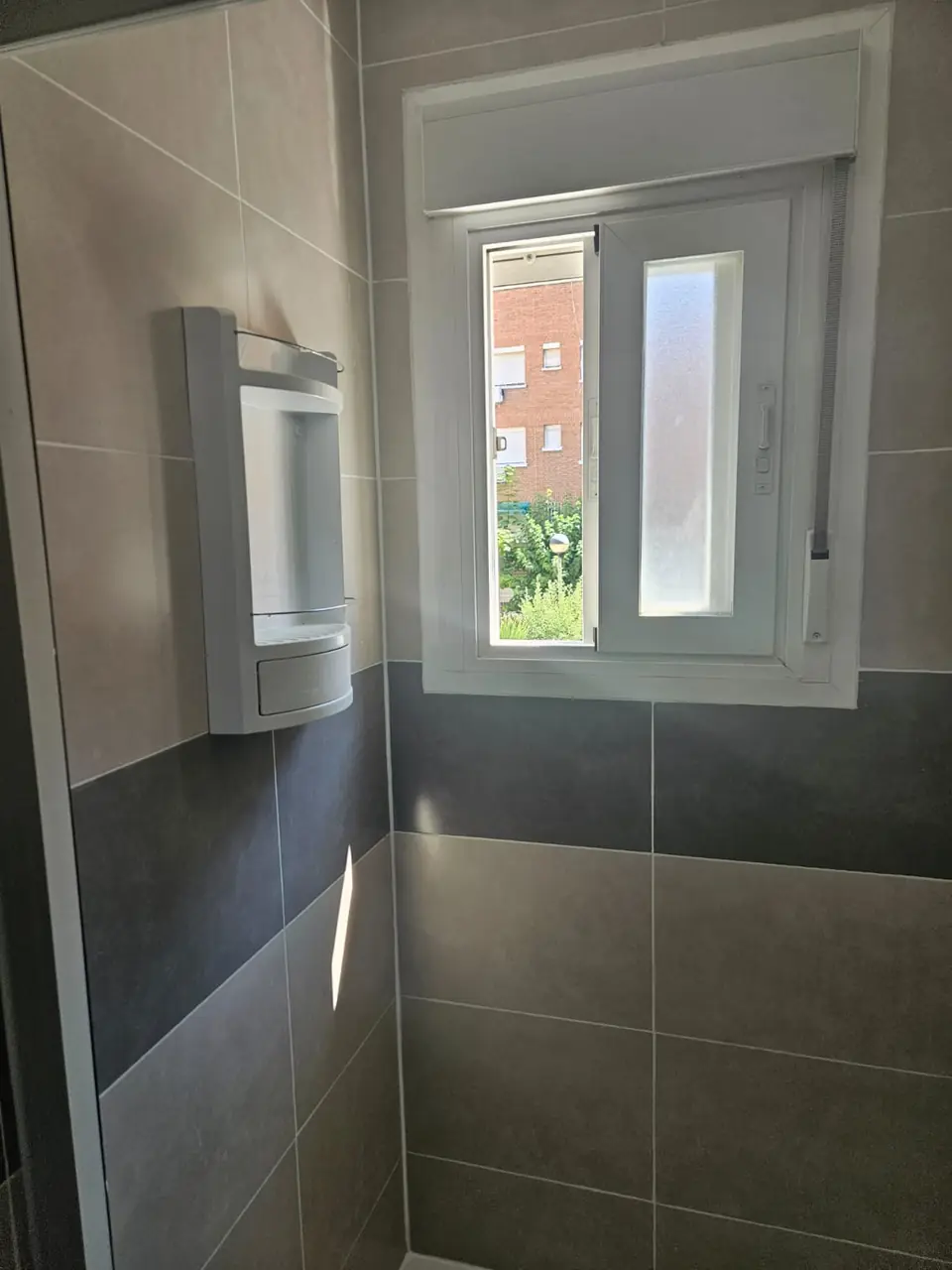 Baño reformado con azulejo de gran formato en dos tonos y ventana nueva de PVC