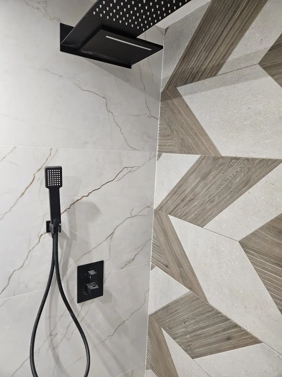 Detalle de ducha con rociador negro mate, teleducha y termostática empotrada sobre porcelánico efecto mármol