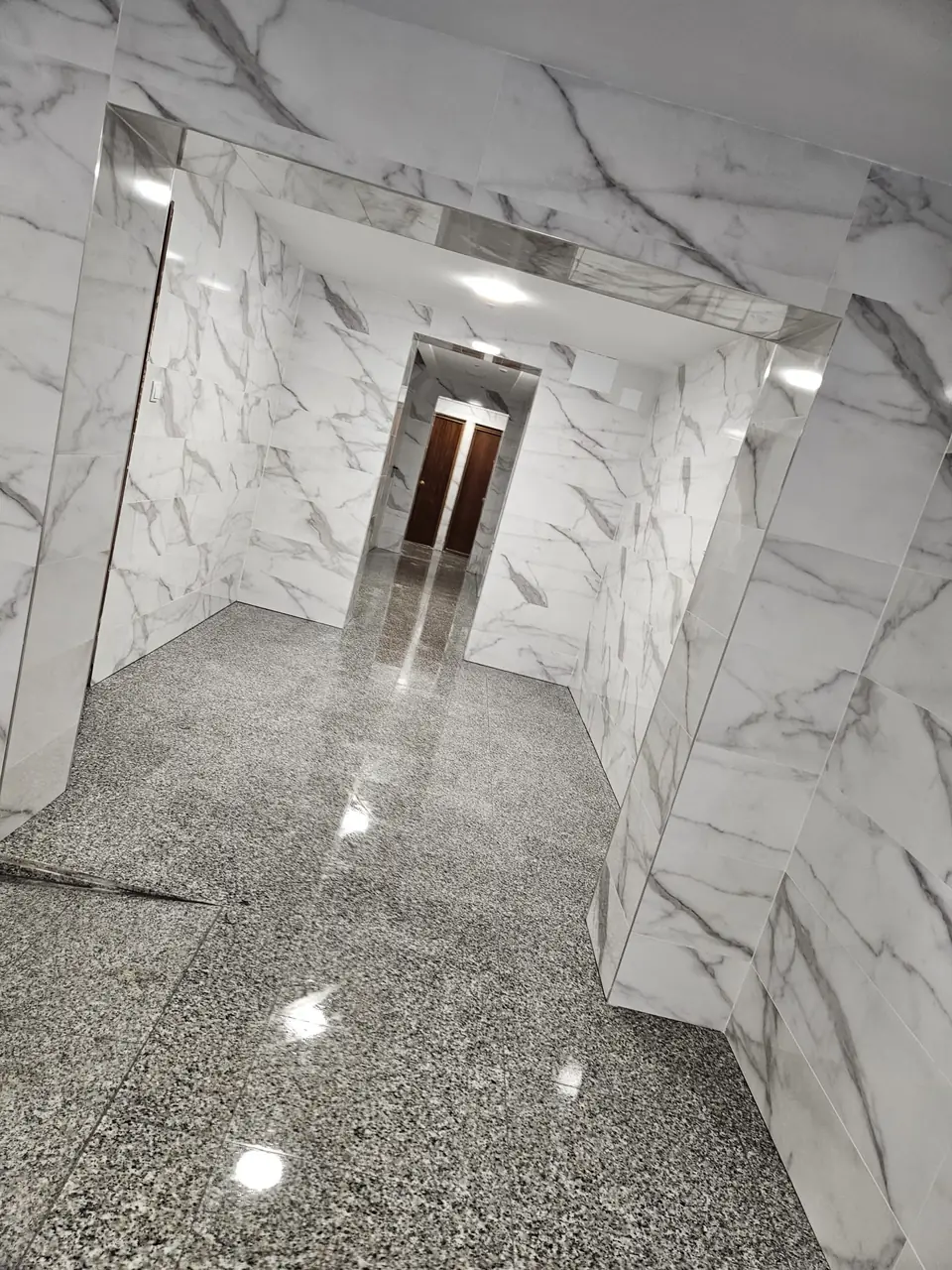 Portal de comunidad de vecinos revestido en porcelánico efecto mármol blanco y suelo de granito pulido
